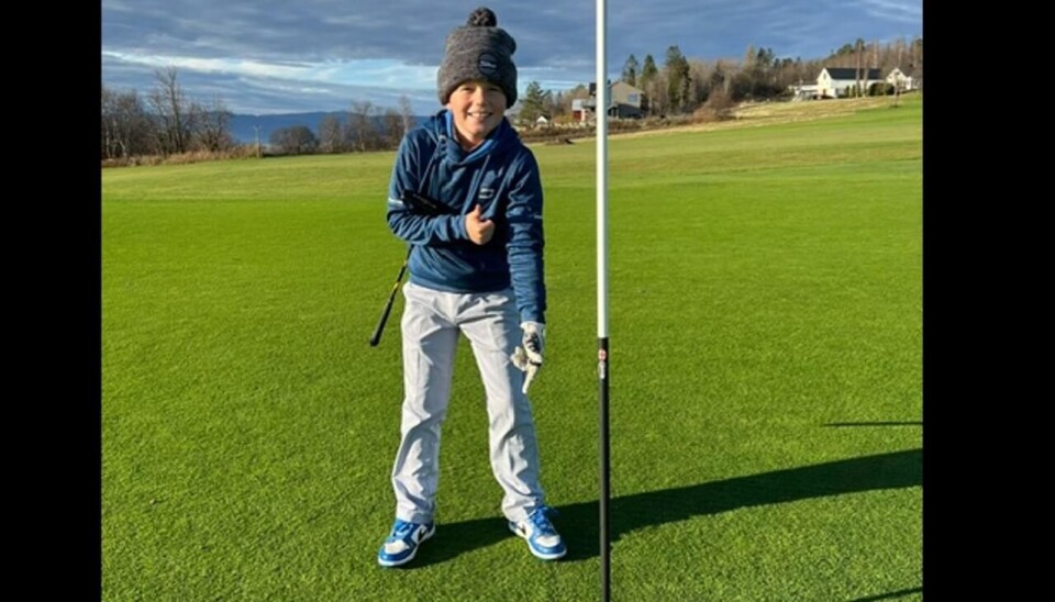En veldig glad William Homstad viser hvor golfballen ligger i koppen etter slaget han slo og fikk sitt første hole-in-one.